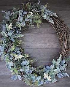 a wreath with greenery and white flowers on a wooden floor in front of a wall