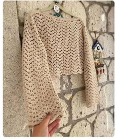 someone is holding up a knitted sweater on a hanger next to a stone wall