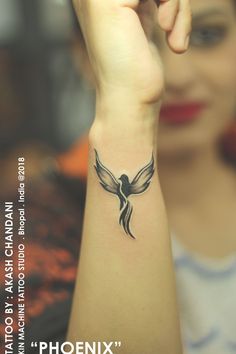 a woman is holding her arm up with a bird tattoo on it's wrist