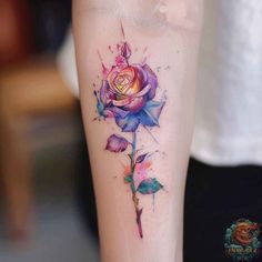 a rose tattoo on the left arm with watercolor paint splatters around it