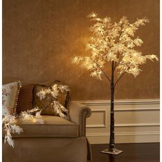 a lighted tree in a living room next to a couch with pillows and throw pillows