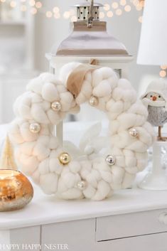 a white wreath sitting on top of a table next to a lamp and other decorations