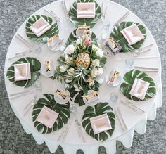 an overhead view of a table set with place settings and tropical leaf napkins on it