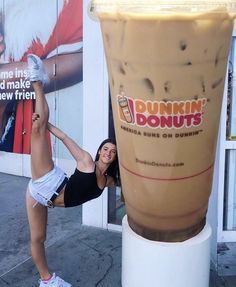 a woman doing a handstand next to a giant drink cup with dunkin'donuts on it