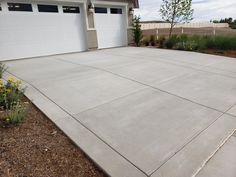 an empty driveway in front of a house with two garage doors and flowers growing on the side