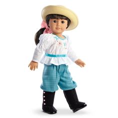 a doll wearing a hat and blue pants with pink bow on her head, standing in front of a white background