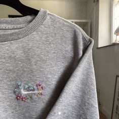 a grey sweatshirt with flowers embroidered on the front and back, hanging from a hanger