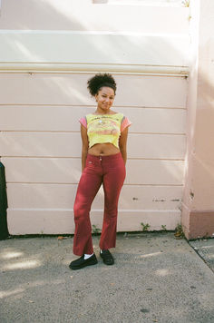 a woman standing in front of a white wall wearing red pants and a yellow crop top