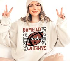 a woman sitting on the floor with her hands up and wearing a sweatshirt that says gameday