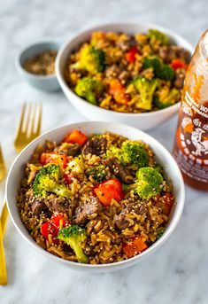 two bowls filled with rice, broccoli and other foods next to a bottle of beer