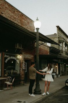 a man standing next to a woman on a street corner near a lamp post and buildings