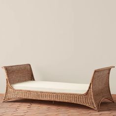 a wicker chaise lounger with white cushions on a brick floor in front of a gray wall