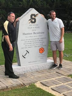 two men standing in front of a stone marker with an orange and white football on it