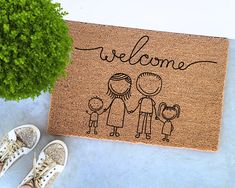 a welcome mat with a family drawn on it next to a potted plant and pair of shoes