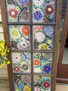 an old window has been decorated with colorful glass flowers and leaves on it's side