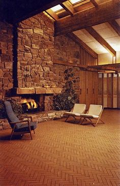 two lounge chairs sitting in front of a fire place inside of a stone wall building