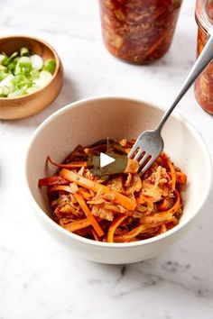 a white bowl filled with shredded carrots next to jars of pickles and sauce