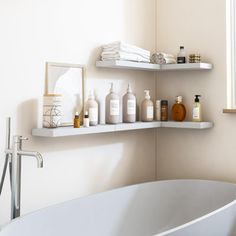 a white bath tub sitting under a window next to a sink and shelves filled with personal care items