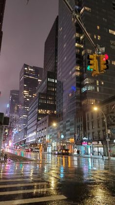 a city street at night with traffic lights and tall buildings in the background on a rainy day