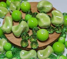 some green apples are on a wooden plate and scattered with other green fruit, as well as leaves