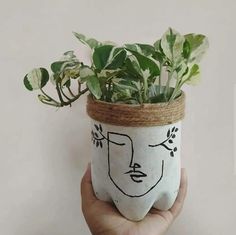 a hand holding a plant in a ceramic pot with a face painted on the side