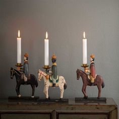 three small figurines are sitting on top of a table with candles in front of them