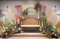 a bench surrounded by plants and flowers in front of a wall with an arched window