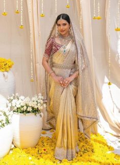 a woman in a yellow sari posing for the camera with flowers on the ground