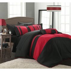 a bed with red and black comforters in a room next to a lamp on a table