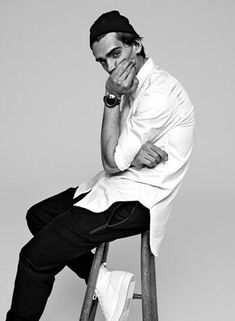 a man sitting on top of a stool with his hands to his face while wearing a white shirt and black pants