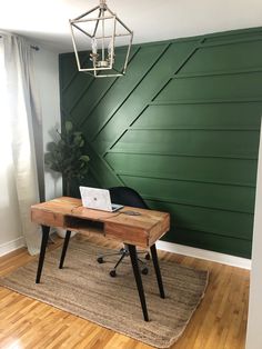 a wooden desk with a laptop on it in front of a green paneled wall