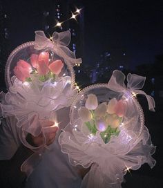 two clear vases with flowers in them are lit up by string lights at night