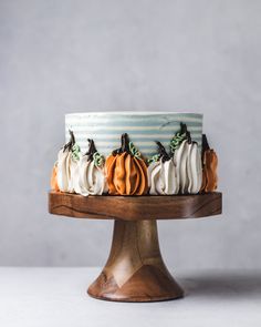 a cake decorated with pumpkins and white frosting on a wooden stand against a gray background