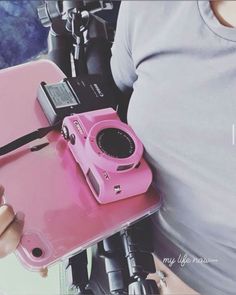 a pink camera sitting on top of a table next to a person holding a cell phone