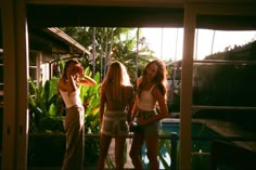 three women are standing in front of a pool talking on their cell phones while the sun shines through the windows