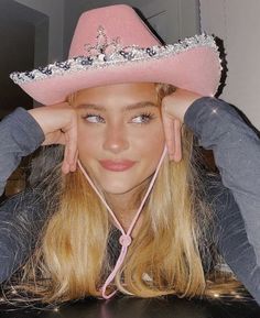 a woman wearing a pink cowboy hat sitting at a table with her hands on her head