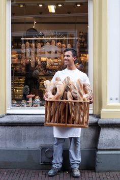 a man standing in front of a store holding a basket full of breads and buns