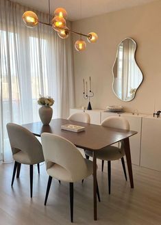 a dining room table with four chairs and a mirror on the wall above it, along with two vases filled with flowers