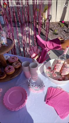 a table topped with plates and cups filled with doughnuts next to pink napkins