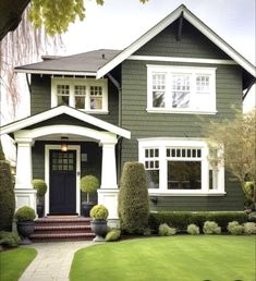 a green house with white trim on the front and side windows, trimmed in boxwood