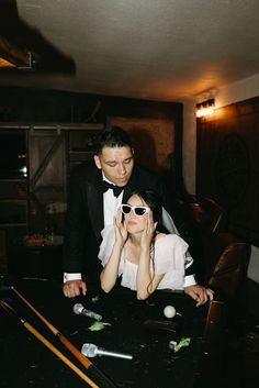 a man in a tuxedo leans over a woman's head as they play pool