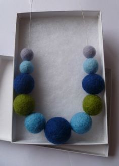 a blue and green beaded necklace in a white box on a table next to a pair of scissors