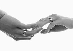 black and white photograph of two people holding hands with wedding rings on their fingers,