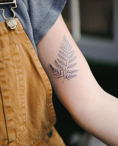 a person with a tattoo on their arm holding onto a piece of paper that has a fern design on it