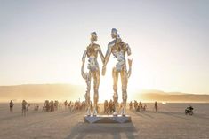 two metal statues standing in the middle of a desert with people walking around and on bikes