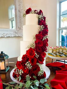 A Four tiered white wedding cake with red roses cascading down the front Red Roses Wedding Reception, Maroon And Gold Wedding Cake, Red Wedding Cake Elegant, Summer Red Wedding, Wedding Red Theme, Red And White Roses Wedding, Roses On Wedding Cake, Red Roses Wedding Cake, Red Roses Wedding Decor