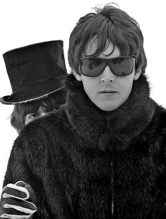 black and white photograph of a man wearing sunglasses and a fur coat with a top hat on his head