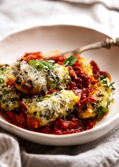 a white bowl filled with spinach and cheese covered ravioli on top of a table