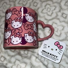 a pink hello kitty coffee mug sitting on top of a bed next to a card