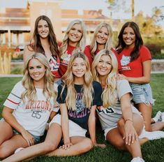 a group of young women sitting on top of a lush green grass covered field next to each other